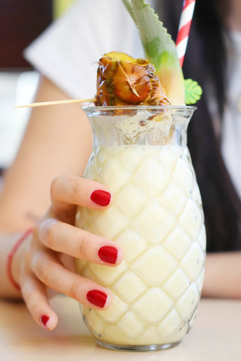Main tenant un cocktail tropical sur glace pilée, illustrant le swizzle cocktail d'été