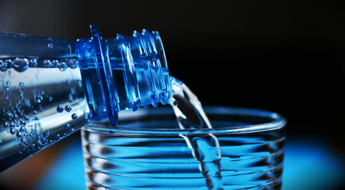 Eau versée d'une bouteille dans un verre, illustration du traitement de l'eau en Horeca
