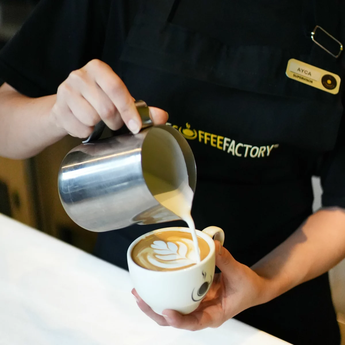 Barista versant du lait pour réaliser un latte art dans une tasse de café