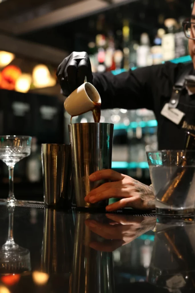 Barman versant un liquide dans un verre au comptoir, geste clé pour doser un sirop simple pour cocktail