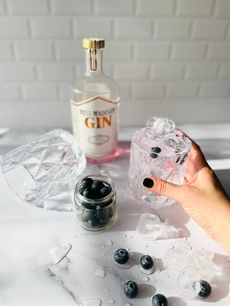 Verre de gin avec myrtilles et glaçons tenu à la main