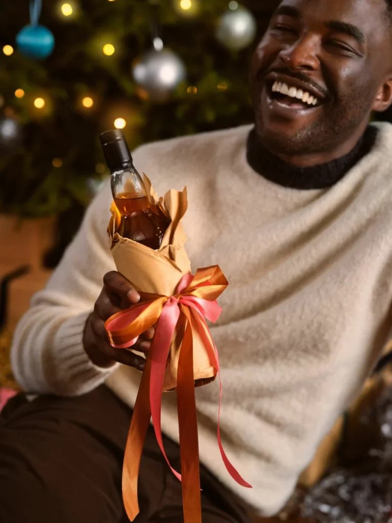 Bouteille de whisky emballée en cadeau, posée au pied d'un sapin