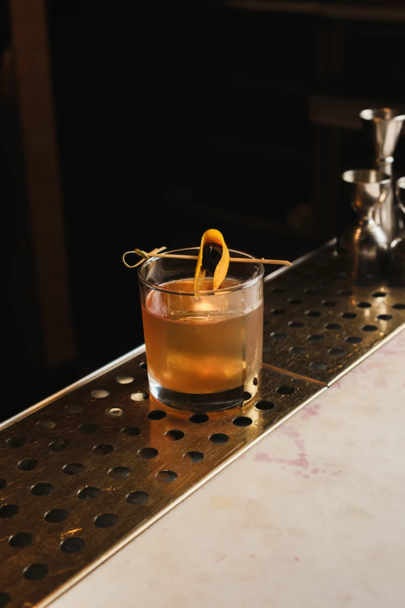 Livre ouvert posé à côté d'un verre de cocktail ambré, atmosphère roman policier