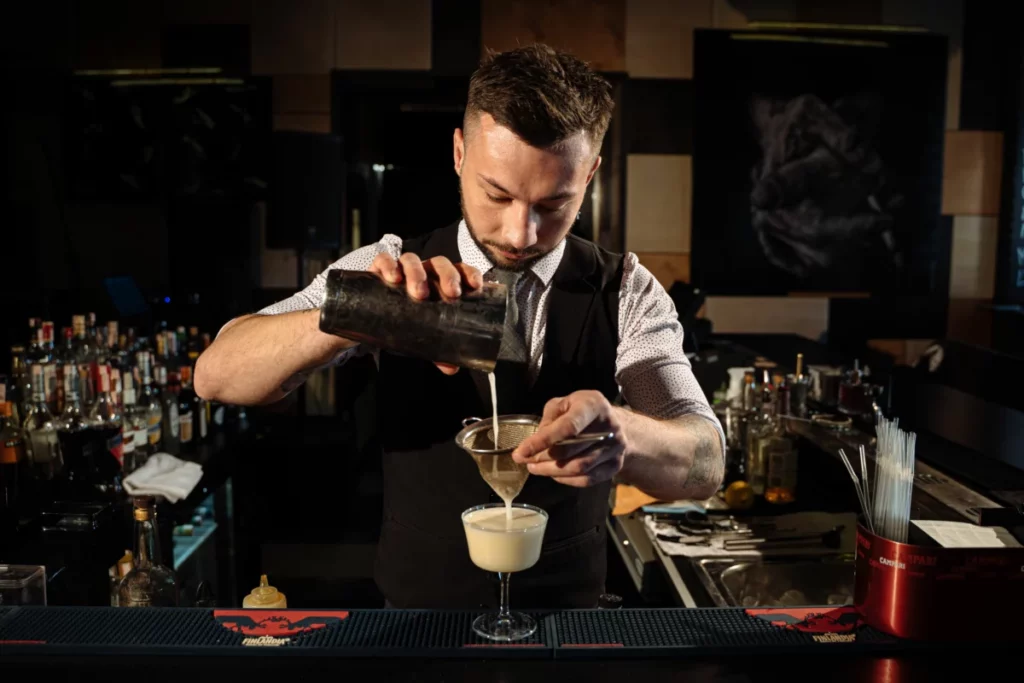 Barman préparant un cocktail derrière son comptoir, à l'issue d'une formation de barman