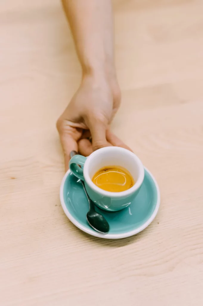 Main tenant une tasse d'espresso sur une table en bois, comme le café signature de Viki Geunes