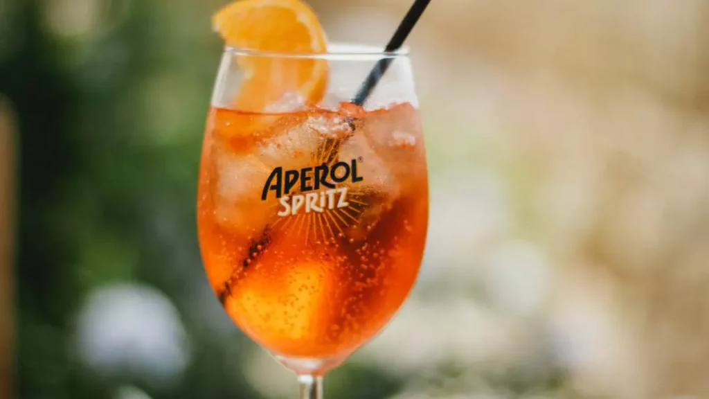 Verre de spritz à l'amaro italien avec glaçons et tranche d'orange posé sur une table en bois