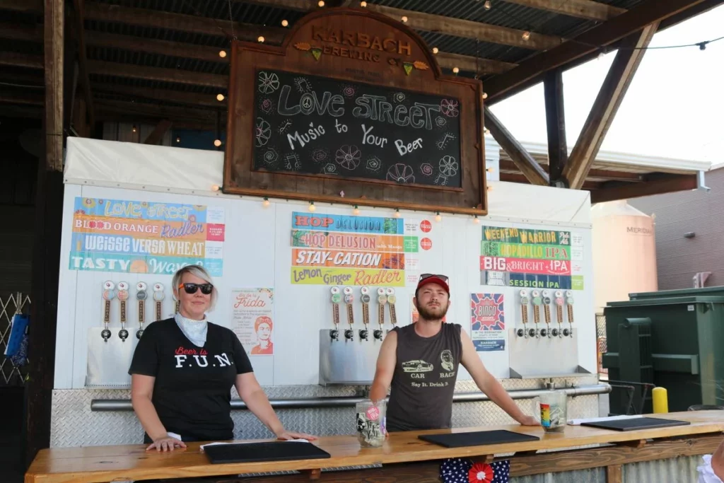 Deux barmen servent des bières artisanales sur un stand extérieur ensoleillé, ambiance du festival Nantes sous Pression 2026