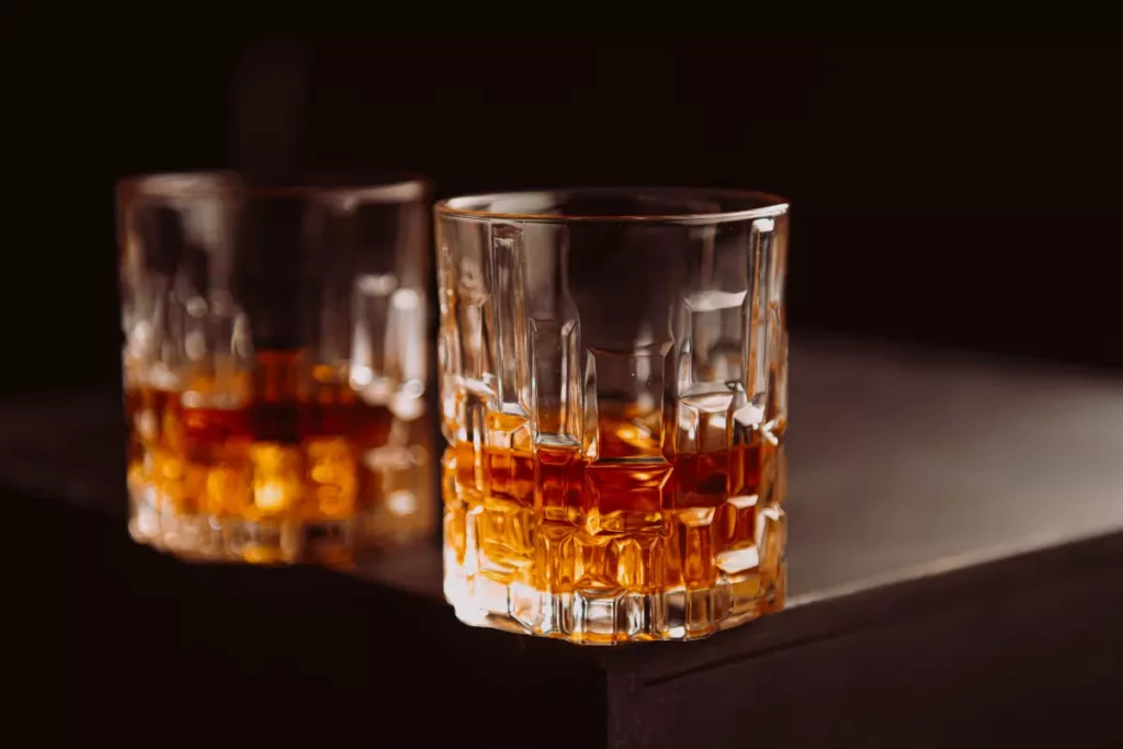 Verres en cristal remplis de whisky ambré sur une table en bois sombre illustrant le Cù Bòcan Creation 9 de la distillerie Tomatin