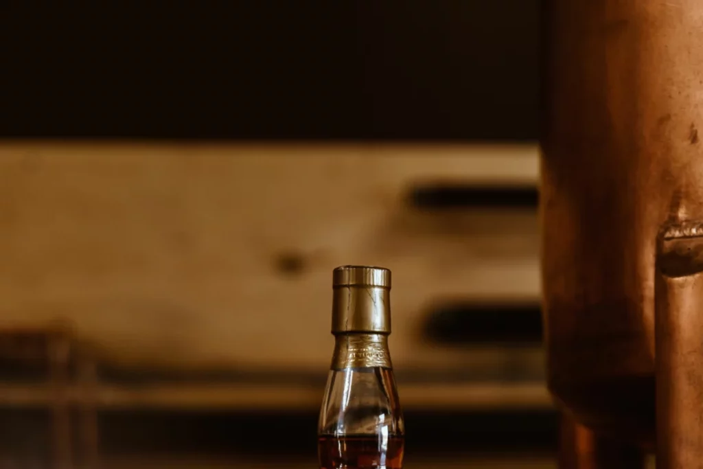 Bouteille de rhum de Martinique AOC vieilli posée sur une étagère en bois devant un alambic en cuivre