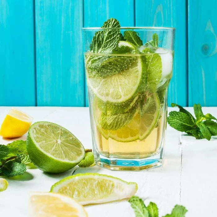 Cocktail Mojito au citron vert et menthe en verre highball sur une table en bois.  Fond bleu.